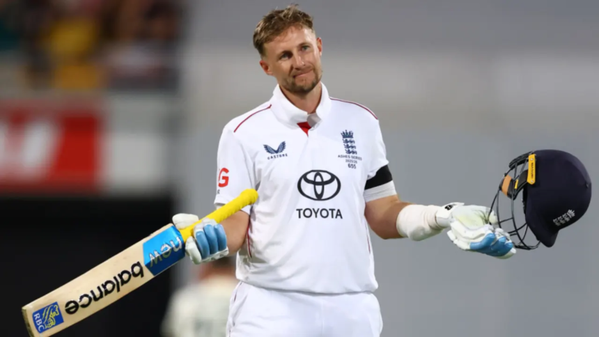 An England cricketer in a white Test uniform stands on the field holding his bat in one hand and his helmet in the other, giving a small shrug with a calm, almost playful expression after completing a milestone innings.