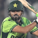 Close-up shot of Pakistan cricket captain Babar Azam batting during a match, wearing the green national uniform, helmet with the star logo, and neon green and white batting gloves, focused on the ball coming towards him.