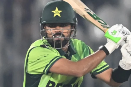 Close-up shot of Pakistan cricket captain Babar Azam batting during a match, wearing the green national uniform, helmet with the star logo, and neon green and white batting gloves, focused on the ball coming towards him.