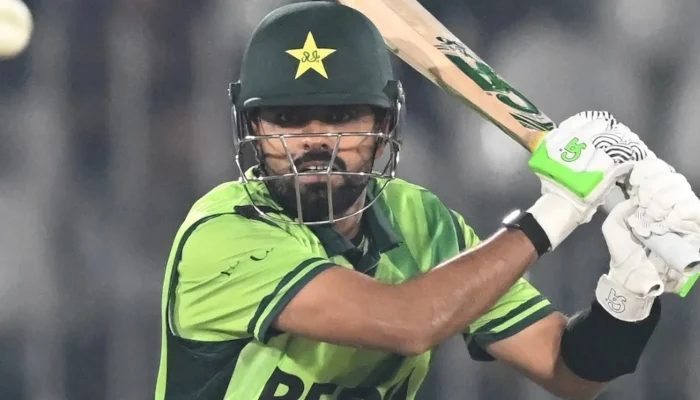 Close-up shot of Pakistan cricket captain Babar Azam batting during a match, wearing the green national uniform, helmet with the star logo, and neon green and white batting gloves, focused on the ball coming towards him.