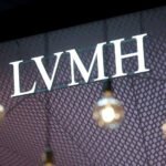 A bright LVMH logo is displayed on a patterned backdrop with hanging lights in the foreground.