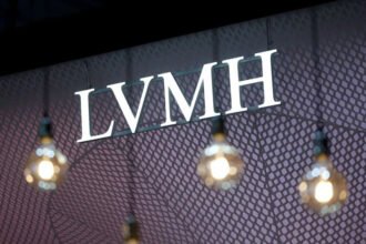 A bright LVMH logo is displayed on a patterned backdrop with hanging lights in the foreground.