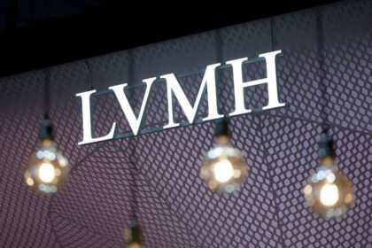 A bright LVMH logo is displayed on a patterned backdrop with hanging lights in the foreground.