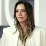 Victoria Beckham wearing a white-and-navy silk midi dress at a NYC holiday event, showcasing her signature quiet-luxury style.