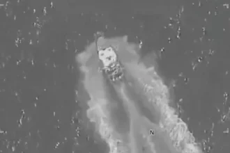 Aerial surveillance image showing a US military strike targeting an alleged drug trafficking boat in the Pacific Ocean, with smoke and wake visible around the vessel.