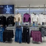 Inside an affordable fashion store in India, sweaters and jeans hang on racks, showing budget pricing as fast fashion and delivery apps reach shoppers in smaller cities.