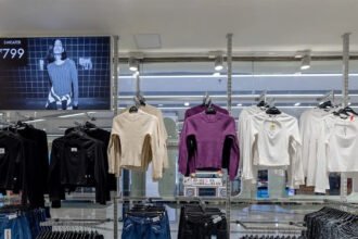 Inside an affordable fashion store in India, sweaters and jeans hang on racks, showing budget pricing as fast fashion and delivery apps reach shoppers in smaller cities.
