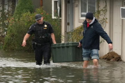 A sheriff helps a resident carry a storage bin through rising floodwater in a residential neighborhood during severe Pacific Northwest flooding.