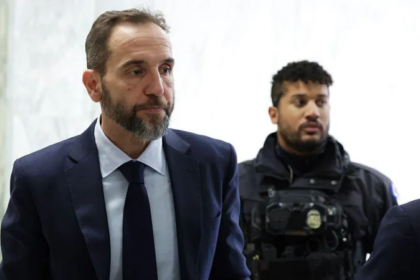 Former special counsel arrives for a closed door congressional hearing, accompanied by a security officer inside a government building