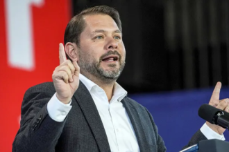 Senator Ruben Gallego speaks at a press conference about legislation to block President Trump from invading Greenland, with U.S. and Greenland flags in the background.