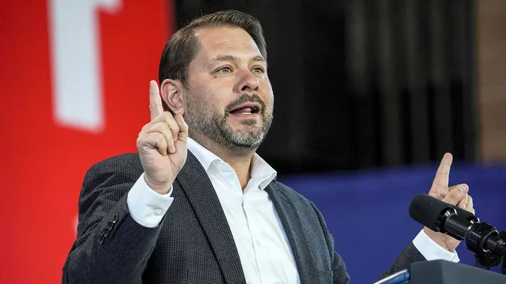 Senator Ruben Gallego speaks at a press conference about legislation to block President Trump from invading Greenland, with U.S. and Greenland flags in the background.
