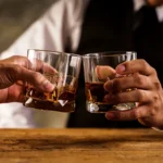 Saudi Arabia has taken a major but quiet step by allowing wealthy foreign residents to legally buy alcohol. This move marks a sharp shift after a nationwide ban that lasted more than seven decades. Observers believe the policy could later include foreign tourists as well. A Discreet Store in Riyadh’s Diplomatic Quarter For many years, Riyadh’s Diplomatic Quarter has felt separate from the rest of the city. The area hosts embassies, luxury housing, green walkways, and cafés popular with young Saudis and expatriates. Inside this exclusive district, an unmarked beige building now serves a new purpose. It houses Saudi Arabia’s first controlled alcohol shop. The store operates quietly and avoids public attention. Officials designed it as a testing ground for easing alcohol restrictions. A Historic Ban Begins to Ease Saudi Arabia banned alcohol sales in 1952. The country is home to Islam’s two holiest sites, which made the ban deeply symbolic. However, the kingdom has changed rapidly in recent years. Under Crown Prince Mohammed bin Salman, the government reopened cinemas and allowed music concerts. Women can now drive. Authorities also limited the power of religious police. The controlled sale of alcohol may be the boldest reform so far. Who Can Buy Alcohol Legally The liquor shop first opened in January 2024. At that time, only non Muslim diplomats could enter. In late 2025, the rules quietly expanded. Now, wealthy non Muslim foreign residents can also shop there. To qualify, an expat must meet one of two conditions. They must hold a Premium Residency permit or earn at least 50,000 Saudi riyals per month. The Premium Residency permit costs 100,000 riyals per year. It usually applies to senior executives, investors, and skilled professionals. Security guards check residence ID cards at the entrance. These cards show both religion and residency status. Expats without the permit must also bring a salary letter from their employer. Tourists remain excluded. Inside the Store Experience Customers say the process feels strict but simple. Staff seal mobile phones in secure bags before entry. Long queues are common and can last over an hour. Inside, shelves carry beer, wine, and spirits. Prices remain high. One British executive said a bottle of whisky cost him 124 dollars. Still, buyers accept the cost because prices remain far lower than black market rates. Several customers spoke anonymously and described the store as well stocked and orderly. What This Change Could Mean This quiet policy shift shows how far Saudi Arabia has moved toward social change. While alcohol remains tightly controlled, the decision signals a softer approach. Many analysts expect gradual expansion, possibly to tourists in the future.