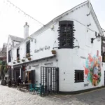 Alasdair Gray Murals on Ubiquitous chip Gain Protected Statute The Ubiquitous chip, one of Glasgow's iconic restaurants, was granted listed building status. This recognition is mainly due to the unique murals painted by the celebrated Scottish artist Alasdair Grey. Historic Environment Scotland officially classifies the building as Category B. The murals in the restaurant are of cultural and artistic importance, as a result. Glasgow Murals that Capture the Creative Spirit Alasdair Grey painted the murals in the early and late 1980s. He was a frequent visitor at the time. In exchange for food and hospitality, he created the art. In the era of that mural, Florid jungle and Arcadia are two rare public works. The vibrant cultural scene in Glasgow's West End is reflected by these works. These works also reflect Gray's strong connection to the local art community. Arcadia shows a group in a garden. This mural features real people from the local community to add a more personal touch. Florid jungle is a colorful and dense natural scene that appears in the courtyard of the restaurant. Cultural Landmarks with Rich History The Ubiquitous chip first opened its doors in 1971. It moved to Ashton Lane, in 1974. The former stables, livery yards and other uses of the building are still evident. It became an important part of Glasgow’s cultural and dining life over time. It was the restaurant that introduced fine Scottish cuisine to the city. The restaurant became a meeting place for writers, artists and performers. Over the years, many well-known people have dined at the restaurant. They include Princess Margaret and Mick Jagger. Greene King purchased the restaurant in 2022 after more than 50-years of family ownership. Gray's Lasting Artistic Legacy Alasdair Grey was born in Glasgow. He became one of Scotland’s most important cultural figures. His work encompassed many different fields including painting, writing and printing. Lanark, his famous novel in Scottish Literature, remains an important landmark. Gray was adamant about bringing art to public places. Gray's work can be found in galleries, pubs, churches and parks all over the city. His work is also on display at the V&A Dundee, and the Scottish National Gallery of Modern Art. Oran Mor is located close to the Ubiquitous Chip. In 2012, a large mural was painted at Hillhead Subway Station. Recognizing the Importance of Public Art Gray, according to experts, wanted to make art available to all. He combines visual art, literature and social concepts in his work. These murals are now protected for future generations. The listing status confirms the importance of these murals in Scotland's culture.