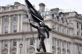 Banksy confirms a new statue in central London at Waterloo Place, showing a suited man with a covered face, placed near historic monuments.