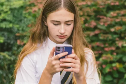 Schools Seek Clear Rules on Proposed Smartphone Ban School leaders and campaigners are asking the government to explain how its planned smartphone ban in schools will work in practice. They say clearer rules are needed so teachers can apply the policy with confidence. The proposal comes through changes to the Children’s Wellbeing and Schools Bill. The government wants schools to treat official guidance as a legal duty. This guidance recommends that schools should be mobile phone free by default. Debate Over How the Ban Should Work During a session in Parliament, Early Education Minister Olivia Bailey said current measures are enough to enforce strong restrictions on phone use in schools. She argued that the system already supports effective bans. However, Shadow Education Secretary Laura Trott agreed with the idea of a ban but questioned how it would be applied. She raised concerns about “not seen, not heard” policies. According to her, such approaches often fail to stop distractions in classrooms. Schools Already Testing Strict Policies Some schools have already introduced their own rules. Rob McGinty, headteacher of Hollingworth Academy in Rochdale, said his school follows a “no see, no hear” policy. Even so, he believes a full ban could work better. He explained that students still bring phones to school. Devices often vibrate or send alerts, which distract students during lessons. This reduces their focus and affects learning. To deal with this, the school is considering lockable pouches. These pouches block signals, so phones cannot receive notifications. This may help students stay focused throughout the day. Challenges in Enforcing a Ban McGinty pointed out a key issue. Even with strict rules, phones can still be hidden in bags or pockets. Notifications can still tempt students to check their devices. He said schools need clearer guidance to manage these situations properly. Delays in Final Decision The legislation is still being debated between the House of Commons and the House of Lords. This process is often called parliamentary “ping pong.” It continues until both sides agree on the final version. Time is becoming a concern for the government. The bill includes other important measures, such as tracking children who are not in school and assigning unique ID numbers to students. These changes may be delayed if the bill is not approved soon.