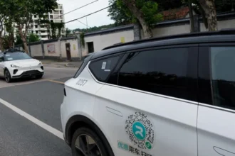Mass Robotaxi Failure Disrupts Traffic in Wuhan What Happened A large-scale robotaxi failure recently disrupted traffic in Wuhan, China. Around a hundred self-driving cars came to a sudden halt in the middle of busy roads. Local authorities confirmed that a system malfunction likely caused the issue. Passengers managed to exit the vehicles safely, and no injuries were reported. Videos shared on social media showed rows of stationary robotaxis, and one clip appeared to capture a minor collision linked to the incident. Police have not confirmed any major damage but continue to investigate the situation. Company Response and Ongoing Investigation The robotaxi service is operated by Baidu through its Apollo Go platform. The company has not yet issued a detailed public response. Authorities stated that the exact cause remains under review. Baidu runs its autonomous taxi service in many cities across China and other regions. The company has played a key role in expanding driverless transport, which makes this disruption especially notable. Growing Safety Concerns Around Driverless Cars Experts say this incident highlights important risks in autonomous systems. Jack Stilgoe, a professor at University College London, noted that driverless technology may reduce accidents overall. However, he added that it can still fail in unexpected ways. The Wuhan outage adds to a series of similar issues. In December 2025, a power failure in San Francisco affected Waymo vehicles and caused widespread traffic delays. Earlier, in Chongqing, an Apollo Go robotaxi fell into a construction pit while carrying a passenger. Future of Robotaxi Technology Despite these challenges, companies like Uber and Lyft continue to explore partnerships with Baidu. They plan to test Apollo Go vehicles in the UK, subject to regulatory approval. Trials are expected to begin in 2026. Experts believe that as autonomous technology grows, governments and companies must focus on new safety standards. These systems still require strong monitoring to prevent failures like the one seen in Wuhan.