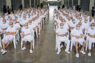 Mass Trial of 486 MS13 Suspects Begins in El Salvador Background of the Case A large scale trial has started in El Salvador involving 486 people accused of belonging to the MS13 gang. Authorities say the suspects are linked to a wide range of serious crimes carried out over a ten year period from 2012 to 2022. Charges and Allegations Prosecutors accuse the group of involvement in more than 47,000 crimes. These include murder, extortion, drug trafficking, arms trafficking, disappearances, and femicide. Officials also say some suspects played roles in violent events in March 2022 when 87 people were killed within a single weekend. Government Response The attorney general’s office says it has strong evidence and expects the court to issue maximum penalties where guilt is proven. The government launched a tough anti gang campaign after the 2022 violence, calling it a war on gangs. Since then, large scale arrests have taken place under a state of emergency that expanded police powers and limited certain constitutional protections. Human Rights Concerns United Nations experts and human rights groups have raised concerns about the trial. They argue that mass proceedings can weaken the right to a fair defense and the presumption of innocence. They also warn that emergency powers have led to possible arbitrary detentions. Despite this, government supporters claim the measures have made the country safer. MS13 Background MS13 is a transnational criminal organization that began in Los Angeles during the 1980s. It was formed by migrants who had fled the Salvadoran civil war. Today, it operates mainly across Central America and has been classified as a terrorist organization by the United States. Legal Process and Current Status Authorities report that 413 suspects are currently in custody, while 73 others are being tried in their absence. The attorney general’s office claims the group has long used violence to control territory and spread fear, affecting both public safety and economic development.