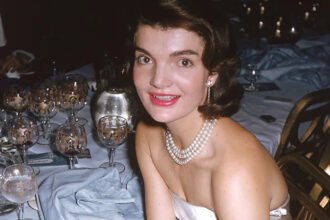 Jackie Kennedy’s 1996 Auction Sparked Public Frenzy The 1996 auction of Jacqueline Kennedy Onassis’s personal belongings turned into one of the most talked-about sales in modern history. Held at Sotheby's in New York, the event drew massive attention from collectors and fans alike. Nearly 1,200 items went up for sale. These included everything from clothing and books to valuable jewelry. What shocked many people was not just the price of items, but the intense public interest. Around 100,000 catalogues were printed, and they quickly sold out. For many buyers, the catalogue itself became a prized keepsake. A Rare Look Into a Private Life Much of the excitement came from curiosity. Jacqueline Kennedy Onassis carefully guarded her personal life. This auction gave people a rare chance to see how she lived behind the scenes. The catalogue featured photos of her home and personal items. These details showed a space that felt warm, elegant, and lived-in. People were not just buying objects. They were connecting with a life that had always seemed distant and refined. A Legacy Linked to History The emotional connection also played a major role. John F. Kennedy’s assassination in Dallas deeply shaped her life and public image. After that tragic moment, she became a symbol of strength and dignity. Many auction items linked back to that period or to the life she rebuilt afterward. This made them more meaningful to buyers. Each piece carried a story tied to a defining chapter in American history. More Than Just an Auction In the end, the auction raised millions of dollars and exceeded all expectations. However, the real story was the public response. People were not simply shopping. They were chasing a connection to a figure who represented grace, style, and mystery. This event showed how powerful a public i