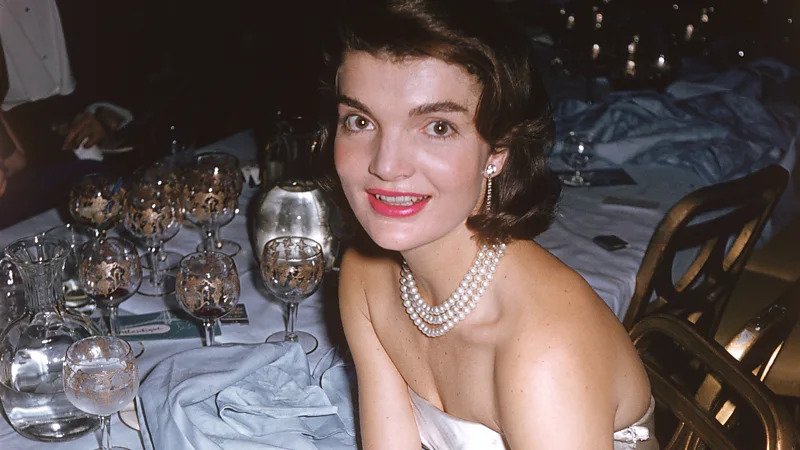 Jackie Kennedy’s 1996 Auction Sparked Public Frenzy The 1996 auction of Jacqueline Kennedy Onassis’s personal belongings turned into one of the most talked-about sales in modern history. Held at Sotheby's in New York, the event drew massive attention from collectors and fans alike. Nearly 1,200 items went up for sale. These included everything from clothing and books to valuable jewelry. What shocked many people was not just the price of items, but the intense public interest. Around 100,000 catalogues were printed, and they quickly sold out. For many buyers, the catalogue itself became a prized keepsake. A Rare Look Into a Private Life Much of the excitement came from curiosity. Jacqueline Kennedy Onassis carefully guarded her personal life. This auction gave people a rare chance to see how she lived behind the scenes. The catalogue featured photos of her home and personal items. These details showed a space that felt warm, elegant, and lived-in. People were not just buying objects. They were connecting with a life that had always seemed distant and refined. A Legacy Linked to History The emotional connection also played a major role. John F. Kennedy’s assassination in Dallas deeply shaped her life and public image. After that tragic moment, she became a symbol of strength and dignity. Many auction items linked back to that period or to the life she rebuilt afterward. This made them more meaningful to buyers. Each piece carried a story tied to a defining chapter in American history. More Than Just an Auction In the end, the auction raised millions of dollars and exceeded all expectations. However, the real story was the public response. People were not simply shopping. They were chasing a connection to a figure who represented grace, style, and mystery. This event showed how powerful a public i