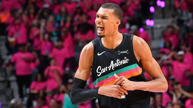 Wembanyama Makes NBA History With Unanimous Defensive Player of the Year Win Historic NBA Defensive Award for Wembanyama Victor Wembanyama of the San Antonio Spurs has won the NBA Defensive Player of the Year award in a historic sweep. Every voter selected him for first place, making him the first player ever to win the award unanimously in its 43 year history. At age 22, he also becomes the youngest player to earn this honor. He is only the second player to win it within his first three NBA seasons, following Spurs legend David Robinson. Wembanyama said he felt proud and very happy, especially about the unanimous support from voters. Dominant Season on Both Ends of the Court Wembanyama led the league in blocks for a third straight season with an average of 3.1 per game. He also posted career highs in scoring at 25 points per game and 11.5 rebounds per game. He added one steal per game, showing strong all around defensive impact. His presence changed how teams attacked the basket. Many opponents avoided the paint when he was on the court because of his shot blocking ability. German basketball legend Dirk Nowitzki praised his impact, saying he has never seen a defender who alters games so strongly just by being on the floor. Spurs Defensive Strength and Team Success The San Antonio Spurs finished the regular season with a 62 wins and 20 losses record. Their defense ranked third in the league, a major factor in their success. Wembanyama also helped push the Spurs into one of the top playoff positions. His performances have made him a strong contender for the Most Valuable Player award as well. Strong Competition in Award Voting Oklahoma City Thunder center Chet Holmgren finished second in voting with 239 points. Ausar Thompson of the Detroit Pistons came third with 60 points. Despite strong competition, Wembanyama secured all first place votes, separating himself clearly from the rest of the field. Playoff Action Around the League The Cleveland Cavaliers took control of their series against the Toronto Raptors with a 115 to 105 win. Donovan Mitchell scored 30 points while James Harden added 28. The Minnesota Timberwolves made a strong comeback against the Denver Nuggets, winning 119 to 114 after trailing by 19 points. Anthony Edwards led with 30 points and 10 rebounds. The Atlanta Hawks also secured an away win over the New York Knicks, taking the game 107 to 106 in a close finish.