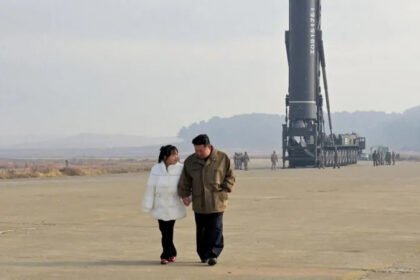 Kim Ju Ae’s Style and What It Signals About North Korea’s Future Leadership Early Public Appearance and Rising Visibility Kim Ju Ae first appeared in state media in November 2022. She was seen standing beside North Korean leader Kim Jong Un during a missile event. She wore a white padded jacket and black trousers. Her hair was neatly tied back. She was very young at the time, believed to be around nine years old. Even then, her appearance looked carefully planned for public display. Increasing Role in State Events Since her first appearance, Ju Ae has been seen more often in public. She now appears at missile tests, military parades, and official ceremonies. Reports suggest she is around 13 years old today. She is no longer shown casually. Each appearance places her close to major military and political moments. This pattern suggests a growing role in state messaging. Clothing as Political Messaging Her clothing choices appear highly controlled. Analysts believe the Propaganda and Agitation Department likely decides her outfits. At times, she wears formal suits and skirts similar to her mother Ri Sol Ju. These outfits create a mature and composed image. They also help reduce attention on her young age. In other appearances, she wears leather jackets and more rugged clothing. These styles match military environments and public events linked to defense activities. Her outfits also visually align with Kim Jong Un, who often wears dark leather jackets and coats. This creates a coordinated family image in public view. Signals of Possible Succession Planning Some South Korean intelligence assessments suggest she may be prepared for a future leadership role. Her growing visibility supports that view. However, experts remain cautious. Her public image may also be part of broader propaganda strategy rather than confirmed succession planning. Key Takeaway Ju Ae’s clothing, presence, and positioning in events appear carefully designed. Her image blends youth with authority. It may reflect how North Korea is shaping public perception around leadership continuity.