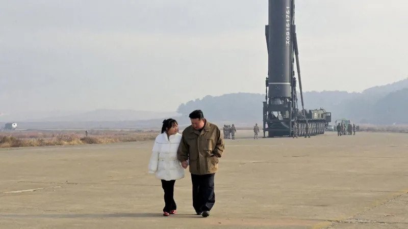 Kim Ju Ae’s Style and What It Signals About North Korea’s Future Leadership Early Public Appearance and Rising Visibility Kim Ju Ae first appeared in state media in November 2022. She was seen standing beside North Korean leader Kim Jong Un during a missile event. She wore a white padded jacket and black trousers. Her hair was neatly tied back. She was very young at the time, believed to be around nine years old. Even then, her appearance looked carefully planned for public display. Increasing Role in State Events Since her first appearance, Ju Ae has been seen more often in public. She now appears at missile tests, military parades, and official ceremonies. Reports suggest she is around 13 years old today. She is no longer shown casually. Each appearance places her close to major military and political moments. This pattern suggests a growing role in state messaging. Clothing as Political Messaging Her clothing choices appear highly controlled. Analysts believe the Propaganda and Agitation Department likely decides her outfits. At times, she wears formal suits and skirts similar to her mother Ri Sol Ju. These outfits create a mature and composed image. They also help reduce attention on her young age. In other appearances, she wears leather jackets and more rugged clothing. These styles match military environments and public events linked to defense activities. Her outfits also visually align with Kim Jong Un, who often wears dark leather jackets and coats. This creates a coordinated family image in public view. Signals of Possible Succession Planning Some South Korean intelligence assessments suggest she may be prepared for a future leadership role. Her growing visibility supports that view. However, experts remain cautious. Her public image may also be part of broader propaganda strategy rather than confirmed succession planning. Key Takeaway Ju Ae’s clothing, presence, and positioning in events appear carefully designed. Her image blends youth with authority. It may reflect how North Korea is shaping public perception around leadership continuity.