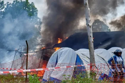 An outbreak of violence erupted at a hospital in eastern Democratic Republic of Congo after the death of a young man suspected of having Ebola. Family members and friends tried to take his body for burial but were stopped by health workers following strict safety rules to prevent infection. The situation quickly escalated. People in the crowd began throwing objects at the facility. Several tents used for isolation and treatment were set on fire. The incident took place at Rwampara General Hospital near Bunia in Ituri province, where most Ebola cases have been recorded. Police responded by firing warning shots to disperse the crowd and regain control of the area. Community reaction and confusion Witnesses said the deceased was a well known local football player. His mother believed he had died from typhoid rather than Ebola, which added to the tension. Local leaders reported that many people in the area do not trust official information about the virus. Some residents believe Ebola is not real or think it is linked to outside organizations and health programs for financial gain. Officials said this lack of trust and awareness is making the response more difficult, especially in remote communities. Medical response and security measures Health workers explained that Ebola burial protocols are essential because the virus remains highly contagious after death. Safe handling of bodies is necessary to prevent further spread. During the unrest, one healthcare worker was injured by stones thrown from the crowd. Medical staff were placed under military protection while security forces restored order at the hospital. Several treatment tents were destroyed in the fire, and at least one body prepared for burial was lost in the chaos. Government response Authorities described the situation as very serious and concerning for public safety. Officials stated that efforts are being increased to improve communication with local communities and to rebuild trust in health services. They emphasized the need for better public awareness so that families understand why strict medical procedures are required during outbreaks.