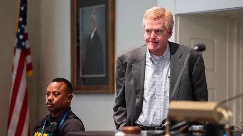 A South Carolina court has overturned the murder conviction of former lawyer Alex Murdaugh. He was convicted in 2023 for killing his wife Maggie and son Paul. The state Supreme Court has now ordered a new trial. Court decision The South Carolina Supreme Court issued a unanimous ruling, 5 to 0, in favor of a new trial. The judges said Murdaugh did not receive a fair trial because of outside influence on the jury. Murdaugh is currently serving two life sentences for the murders. He is also serving additional prison terms for financial crimes at both state and federal level. Reason for new trial The court found that the Colleton County Clerk of Court, Rebecca Hill, improperly influenced the jury. The judges said her actions affected the fairness of the trial. Hill has already pleaded guilty to misconduct, obstruction of justice, and perjury. She admitted to sharing sealed information and misusing public funds. Claims of jury influence The ruling included statements from jurors who said Hill made comments during the trial. One juror said she was told to watch Murdaugh closely, which affected how she viewed the case. Other jurors reported being told not to trust the defense and to avoid being misled by evidence presented in court. Some also said Hill suggested the case should not take long during deliberations. Background of the case Murdaugh was once a powerful attorney in South Carolina. His criminal trial lasted six weeks and received global attention. The case involved the shooting deaths of his wife and son near the family property. After his conviction, the case became widely covered through documentaries, podcasts, and books. The trial was also broadcast publicly. Hill later published a book about the case, but it was later withdrawn after plagiarism concerns.