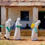Police Fire Warning Shots as Crowds Gather at DR Congo Ebola Treatment Centre Tensions rose in eastern Democratic Republic of the Congo after police fired warning shots into the air to break up angry crowds outside an Ebola treatment centre in Mongwalu. Families reportedly tried to take back the bodies of relatives who had died from the deadly virus. Health officials said the unrest continued for several hours on Sunday. The treatment centre had already faced an overnight attack earlier in the weekend when unknown people set fire to an isolation tent inside the hospital compound. Families Demand Bodies of Victims According to hospital officials, several people gathered outside the medical facility demanding that authorities release the bodies of two Ebola victims to their families for burial. One of the victims was reportedly a respected Catholic religious leader known in the local community. Doctors warned that Ebola victims remain highly infectious after death. Traditional funeral practices and direct contact with bodies can quickly spread the virus to more people. Medical teams and Red Cross workers have been carrying out controlled burials under police protection to reduce the risk of further infections. Fear and Distrust Fuel Public Anger Many communities affected by the outbreak continue to distrust health authorities. Some residents question the real cause of deaths and remain skeptical about Ebola treatment measures. Earlier in the week, another violent incident took place in Rwampara, a town located southeast of Mongwalu. Protesters burned isolation tents after officials stopped them from removing the body of a suspected Ebola victim for a traditional burial ceremony. Health experts believe misinformation and fear are making it harder to control the outbreak. Ebola Cases Continue to Rise Officials say the current Ebola outbreak has now recorded more than 900 suspected cases and around 220 suspected deaths. The situation has raised concern across Central and East Africa. Red Cross officials also confirmed that three volunteers involved in handling dead bodies died from suspected Ebola infections. Their deaths highlight the dangers faced by frontline workers during the outbreak. Meanwhile, health ministers from Uganda, South Sudan, and the Africa Centres for Disease Control and Prevention recently agreed to strengthen cross border cooperation to help stop the virus from spreading into neighboring countries. Why Safe Burials Matter During Ebola Outbreaks Health experts say safe burials remain one of the most important steps in controlling Ebola outbreaks. The virus can survive in the bodies of victims after death, making funeral gatherings extremely risky. Authorities continue to urge families to cooperate with medical teams to protect communities and prevent more infections.