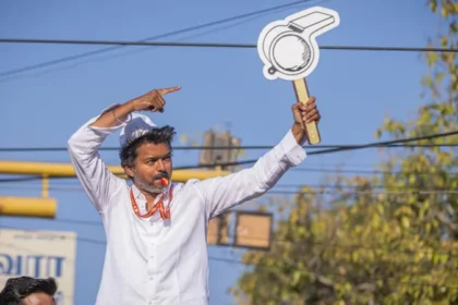 Political uncertainty in Tamil Nadu after actor Vijay’s party falls short of majority Historic win but no clear mandate C Joseph Vijay, a well known film star turned politician, has led his newly formed party Tamilaga Vettri Kazhagam (TVK) to a major breakthrough in Tamil Nadu’s state election. The party won 108 seats in the 234 member assembly, becoming the single largest party. However, it still fell 10 seats short of the 118 needed for a majority. This result created a hung assembly, leaving the state without a clear path to form a stable government. Coalition talks begin amid uncertainty After the results, the Indian National Congress, holding five seats, announced its support for TVK. Even so, Vijay still needs at least five more legislators to reach the majority mark. He met Tamil Nadu Governor Rajendra Vishwanath Arlekar and formally staked claim to form the government. The governor later stated that TVK has not yet shown proof of majority support in the assembly. Reports suggest the governor has asked Vijay to demonstrate backing from at least 118 members before any invitation to form government is considered. Debate over constitutional process TVK leaders and allies have criticized the governor’s approach, arguing that the single largest party should normally be given a chance to prove majority on the assembly floor. Legal and constitutional experts remain divided. Some say the governor is acting to ensure political stability, while others believe established convention supports inviting the largest party first and allowing a floor test later. A shift in Tamil Nadu politics TVK’s rise has been compared to earlier political disruptions in the state, especially when MG Ramachandran broke away to form AIADMK and later became chief minister. For decades, Tamil Nadu politics has been dominated by DMK and AIADMK. This election broke that pattern, with TVK emerging as the strongest single party and defeating the ruling DMK. Possible outcomes still open In the past few days, political discussions have intensified. There is even speculation about unlikely alliances between long time rivals. However, analysts say Vijay may still secure support from smaller parties and independents to reach the required number. The final outcome now depends on post election negotiations, not just the vote results.