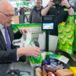 Swinney Defends Food Price Cap Plan Ahead of First Minister Vote SNP Leader Promises Relief for Families Facing Rising Food Costs John Swinney has defended his proposal to cap the prices of essential food items as he prepares for a key vote to remain Scotland’s first minister. He said the policy focuses on helping families manage the ongoing cost of living crisis rather than creating political conflict with the UK government. Speaking ahead of the parliamentary vote, Swinney explained that many households continue to struggle with the rising cost of groceries. According to him, the government has a responsibility to make healthy and basic food items more affordable for the public. Under the proposed SNP plan, major supermarkets in Scotland would have to limit the prices of up to 50 everyday products. These products could include milk, eggs, rice, cheese, and other household essentials. The policy aims to reduce pressure on low and middle income families who are finding it difficult to keep up with food expenses. Supermarkets and Retailers Raise Concerns The proposal has already sparked debate among retailers and business groups. The Scottish Retail Consortium criticized the plan and called it unrealistic. Retail representatives warned that smaller stores could struggle to compete because the price cap would mainly target large supermarket chains. Business leaders also argued that limiting prices could create challenges for suppliers and retailers. However, Swinney responded by saying the government would work closely with supermarkets, producers, and other stakeholders before finalizing the legislation. He stressed that public support remains his main concern because many people across Scotland continue to face financial hardship. Swinney added that discussions with retailers would play an important role in making the policy practical and effective. UK Law Could Create Challenges The SNP leader admitted that introducing the food pricing law may require cooperation with the UK government. Experts believe the proposal could conflict with the UK Internal Market Act 2020, which was introduced after Brexit to prevent trade barriers between Scotland, England, Wales, and Northern Ireland. Since the SNP no longer holds a parliamentary majority, Swinney acknowledged that he would need support from opposition parties in Holyrood as well as discussions with ministers in Westminster. Despite criticism from political opponents, Swinney rejected claims that the policy was designed to trigger a political dispute with London. Instead, he insisted that his goal is to support people who are struggling to afford basic shopping needs. Additional Promises in SNP Manifesto Alongside the food pricing proposal, the SNP has also promised to introduce a £2 cap on bus fares and expand childcare services across Scotland. The party says these measures would help reduce financial pressure on working families and improve access to affordable public services. Swinney believes the combined policies would provide direct support to households dealing with inflation and rising living costs.