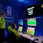 # FIFA Investigates VAR Official's Hand Gesture Before Germany's World Cup Match FIFA has launched an inquiry after video assistant referee Shaun Evans made a hand gesture during the pre-match broadcast of Germany's World Cup clash against Curacao. The incident occurred moments before Germany secured a dominant 7 to 1 victory on Sunday. During the official World Cup broadcast, cameras briefly introduced the refereeing team and the VAR officials working from the referee operations hub in Dallas. While the camera focused on the VAR room, Evans appeared to make an upside-down "OK" hand sign. Viewers quickly noticed the gesture, and discussions spread across social media platforms. Many users questioned its meaning and whether it carried any controversial message. ## FIFA Requests Clarification Sources indicate that FIFA is seeking an explanation from the Australian official regarding the gesture. The governing body has not yet released a formal public statement. The incident attracted widespread attention because the hand sign can have different interpretations. Some viewers believed it was harmless, while others linked it to more concerning symbolism. Following the controversy, broadcasts of later World Cup matches appeared to change their presentation style. Instead of facing the camera, VAR officials remained focused on their monitors during pre-match introductions. ## What Does the Upside-Down OK Sign Mean? The upside-down "OK" sign has several possible meanings. One common interpretation comes from the popular "circle game." In this prank, a person forms the symbol below their waist. If someone looks directly at it, they lose the game and may receive a playful punch on the shoulder. The gesture gained popularity through internet culture and television shows before becoming a widely recognized online meme. However, the symbol has also been associated with far-right groups in recent years. Anti-discrimination organizations have noted that some extremists adopted the sign as a way to communicate with supporters or attract attention online. Because of these associations, the gesture has become controversial in certain contexts. ## Anti-Discrimination Groups Seek Answers Several organizations that monitor discrimination and racism in football have requested further clarification about the incident. Experts from anti-discrimination groups stated that the gesture closely resembles a symbol that has been used within some far-right circles. As a result, they believe the matter deserves careful review. The incident has renewed discussions about the importance of maintaining inclusive standards at major international sporting events. ## Experienced Official Under Scrutiny Shaun Evans is one of Australia's most experienced football officials. He has served on FIFA's international referees list since 2017 and has worked at major tournaments, including the 2022 FIFA World Cup. He has also officiated in Australia's top professional league for many years and previously handled a national championship final. As FIFA continues its review, football fans and anti-discrimination groups await further clarification regarding the meaning and intent behind the gesture.