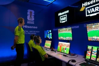 # FIFA Investigates VAR Official's Hand Gesture Before Germany's World Cup Match FIFA has launched an inquiry after video assistant referee Shaun Evans made a hand gesture during the pre-match broadcast of Germany's World Cup clash against Curacao. The incident occurred moments before Germany secured a dominant 7 to 1 victory on Sunday. During the official World Cup broadcast, cameras briefly introduced the refereeing team and the VAR officials working from the referee operations hub in Dallas. While the camera focused on the VAR room, Evans appeared to make an upside-down "OK" hand sign. Viewers quickly noticed the gesture, and discussions spread across social media platforms. Many users questioned its meaning and whether it carried any controversial message. ## FIFA Requests Clarification Sources indicate that FIFA is seeking an explanation from the Australian official regarding the gesture. The governing body has not yet released a formal public statement. The incident attracted widespread attention because the hand sign can have different interpretations. Some viewers believed it was harmless, while others linked it to more concerning symbolism. Following the controversy, broadcasts of later World Cup matches appeared to change their presentation style. Instead of facing the camera, VAR officials remained focused on their monitors during pre-match introductions. ## What Does the Upside-Down OK Sign Mean? The upside-down "OK" sign has several possible meanings. One common interpretation comes from the popular "circle game." In this prank, a person forms the symbol below their waist. If someone looks directly at it, they lose the game and may receive a playful punch on the shoulder. The gesture gained popularity through internet culture and television shows before becoming a widely recognized online meme. However, the symbol has also been associated with far-right groups in recent years. Anti-discrimination organizations have noted that some extremists adopted the sign as a way to communicate with supporters or attract attention online. Because of these associations, the gesture has become controversial in certain contexts. ## Anti-Discrimination Groups Seek Answers Several organizations that monitor discrimination and racism in football have requested further clarification about the incident. Experts from anti-discrimination groups stated that the gesture closely resembles a symbol that has been used within some far-right circles. As a result, they believe the matter deserves careful review. The incident has renewed discussions about the importance of maintaining inclusive standards at major international sporting events. ## Experienced Official Under Scrutiny Shaun Evans is one of Australia's most experienced football officials. He has served on FIFA's international referees list since 2017 and has worked at major tournaments, including the 2022 FIFA World Cup. He has also officiated in Australia's top professional league for many years and previously handled a national championship final. As FIFA continues its review, football fans and anti-discrimination groups await further clarification regarding the meaning and intent behind the gesture.
