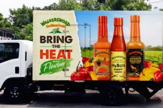 Caribbean Hot Sauce Industry Hit by Scotch Bonnet Pepper Shortage Key Ingredient Under Pressure Hot sauce is a daily essential across Caribbean households. Scotch bonnet peppers give it the signature heat found in meals like rice and peas, curries, and stews. Demand for Caribbean hot sauce has also grown internationally. These products now appear in major supermarkets in the United States, United Kingdom, and Australia. However, producers are now struggling to keep up with supply because the main ingredient is becoming harder to source. Weather Damage Disrupts Farming Farmers in Jamaica, a major Scotch bonnet producing country, have faced repeated setbacks from extreme weather. Recent hurricanes caused serious damage to farmland and crops. Heavy rainfall also affected plant growth and reduced pepper quality. In some cases, excess rain reduced the heat level of the peppers, which directly impacts sauce flavour. Farmers also deal with plant diseases and pests that weaken harvests and reduce yields. Because of these combined pressures, production has dropped and supply has tightened. Farmers Switch Crops for Stability Many farmers have reduced Scotch bonnet cultivation after repeated losses. Some have shifted to crops like sweet potatoes because they are more stable and offer better financial security. This shift has reduced the overall supply of Scotch bonnet peppers even further, making it harder for sauce manufacturers to maintain production levels. Rising Prices and Supply Challenges Hot sauce manufacturers report major cost increases due to limited pepper availability. Some producers say pepper prices rose sharply after major storms, with increases reaching around 10 times in the short term. Over the last two years, costs have climbed by roughly 40 to 50 percent. Companies that rely heavily on exports have also been forced to cancel orders when supply runs low. To manage shortages, some businesses are increasing storage of peppers throughout the year. This helps reduce sudden supply gaps but adds extra cost and risk. Cultural Importance and Industry Impact Scotch bonnet peppers hold strong cultural value in Jamaica and across the Caribbean. They are used in nearly every type of local cooking and are a core part of national identity. Hot sauce producers say demand remains strong both locally and abroad, but supply instability is now their biggest challenge. As climate conditions continue to change, the industry faces ongoing uncertainty about future harvests and pricing stability.
