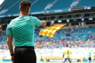 FIFA Introduces New Semi Automated Offside Technology for 2026 World Cup Faster Offside Decisions with Real Time Alerts FIFA will roll out an upgraded semi automated offside system at the 2026 World Cup. The aim is to speed up VAR decisions and reduce long stoppages during matches. Assistant referees will now receive instant audio alerts when a player is more than 10cm offside. This update means the assistant does not always need to wait for play to fully continue before reacting. However, the assistant referee still controls when to raise the flag and stop the game. How the New System Works The new technology builds on earlier versions tested at major tournaments such as the Club World Cup and the Intercontinental Cup. Earlier systems only triggered alerts when a player was clearly offside by more than 50cm. The updated version increases precision and reacts to tighter margins. FIFA has also added safeguards. If there is any suspicion of a technical fault, officials can ignore the alert and rely on standard judgment. Limits of the Technology The system does not solve every offside situation. It still struggles with very tight calls where players are almost level. It also becomes less reliable when players are on the ground or when multiple players are close together. It is designed only for positional offside decisions. It cannot decide subjective cases, such as whether a player interfered with an opponent without touching the ball. AI Player Scanning and 3D Models FIFA will also use AI powered 3D avatars of every player at the tournament. All 1,248 players across the 48 teams will be digitally scanned during pre tournament sessions. Each scan takes about a second and is done once during official photo shoots. These digital models will help produce clearer and more accurate offside graphics for TV broadcasts. Safety Concerns Behind the Change The move also responds to concerns about delayed flags and player safety. In one serious incident in 2025, Nottingham Forest striker Taiwo Awoniyi suffered a severe injury after a delayed offside decision led to continued play. FIFA hopes faster alerts will reduce these risks and prevent unnecessary collisions during live play. What Fans Can Expect At the 2026 World Cup, fans should see quicker decisions, fewer long VAR pauses, and clearer offside visuals on screen. The goal is a smoother viewing experience with fewer controversial delays.