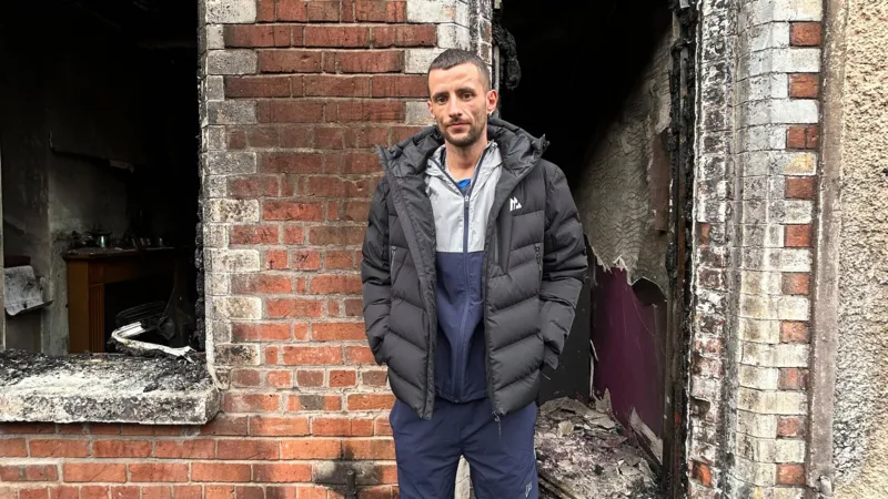 Home Lost in Belfast Fire as Resident Says He Will “Never Get Over” Watching It Burn Residents flee after overnight violence in east Belfast Families in Belfast were forced to leave their homes during a night of unrest that followed a knife attack on Monday. Several houses across the city were damaged after fires broke out during the disorder. Among those affected was a family with a two month old baby, who had to escape as the situation escalated. East Belfast home destroyed in blaze A man from Lendrick Street in east Belfast said he lost the house he had lived in for 13 years after it was set on fire during the chaos. He said the fire began after a nearby car, linked to foreign nationals, was ignited. The flames then spread quickly, leaving little time for firefighters to save the property. By the time emergency crews arrived, the house was already fully burning and could not be saved. “I’ll never get over it,” says homeowner Speaking outside the remains of his home, the man said the experience left him devastated. He described the moment he watched the house burn as something he would carry with him for life. He said the property held many personal and sentimental items that cannot be replaced. Although he expressed anger about the wider violence, he questioned what the destruction had achieved and said it only harmed the local community further. Community impact and ongoing concern The unrest has left several families displaced and facing major losses. While no one from the affected household was injured, the emotional and financial damage is severe. The resident said he was relieved his children were not inside the house at the time of the fire.
