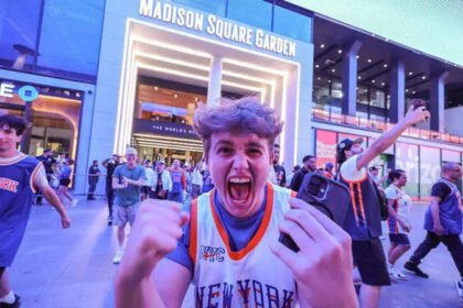Knicks Bring Championship Fever Back to New York The New York Knicks have ignited a wave of excitement across New York City after reaching the NBA Finals for the first time since 1999. The team now leads the series 2 to 0 against the San Antonio Spurs, putting them just two wins away from a long awaited championship title. Game three takes place at Madison Square Garden, marking the first home game of the series. Fans across the city are treating it like a historic moment. High Security at Madison Square Garden Security has been significantly increased for the high profile game. Fans will face strict no bag rules along with airport like screening before entering the arena. US President Donald Trump is expected to attend the match, alongside New York Mayor Zohran Mamdani. The event has also attracted major celebrities including Timothée Chalamet, Ben Stiller, and Spike Lee. Authorities are preparing for heavy crowds and strong public attention due to the high stakes nature of the game. New York City Turns Orange and Blue The city has fully embraced the Knicks playoff run. Famous landmarks such as the Empire State Building and One World Trade Center have lit up in the team colors. Subway stations near Madison Square Garden now feature Knicks themed decorations. Local businesses across the five boroughs are offering special food deals, including orange and blue inspired snacks and desserts. Bars and public spaces are packed on game nights, with fans gathering to watch live broadcasts. Many streets near the arena have turned into unofficial celebration zones. Fans Celebrate a Historic Turnaround The Knicks success this season has surprised many supporters after years of poor performance. The team now stands one step away from a potential first championship since 1973. Even during away games in Texas, thousands of fans gathered in New York to celebrate wins. Some of these gatherings led to crowd control issues and several arrests as celebrations grew intense. Despite this, the atmosphere across the city remains highly energetic and focused on the possibility of a title win.