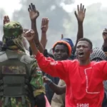 Protest Turns Violent in Nanyuki A protest in Nanyuki, a town in Kenya, turned deadly when clashes broke out between demonstrators and police over a planned Ebola isolation facility for US citizens. Witnesses reported that a man was shot during the unrest and later died. Authorities have not released an official statement on the incident. Earlier in the day, protesters gathered with Kenyan flags, placards, and even a symbolic coffin labeled Ebola. They demanded that the project be cancelled immediately. Subheading 2: Rising Tensions and Police Response Police used tear gas to disperse crowds as the demonstration escalated. Witnesses described chaos in the streets, with gunfire reported during the confrontation. According to journalists at the scene, one man was seen lying motionless after being shot. Local reports also say that similar protests in recent weeks ended in fatalities, increasing public anger and mistrust. Subheading 3: Concerns Over US Health Facility Plan The planned facility is expected to be a fifty bed isolation centre at a military base. It is designed to treat US citizens affected by an Ebola outbreak in Central Africa. Residents and protest leaders argue that the project lacks transparency and could put local communities at risk. Many fear possible disease exposure and say they were not properly consulted. Subheading 4: Legal Challenge and Public Reaction A court had already ordered a temporary halt to the project after a rights group raised concerns about public health risks. The case continues to fuel debate in the region. One protester said the project has created fear in the area and reduced visits to the county. Community members insist that their concerns must be addressed before any construction continues. Subheading 5: Background of the Ebola Situation The Ebola outbreak in parts of Central Africa has already led to hundreds of confirmed cases and over a hundred deaths. The proposed facility in Kenya is meant to support faster medical response for infected US nationals. A US official stated that Kenya was selected due to regional travel access and limited medical capacity in nearby airports.