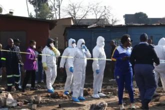 Police Launch Manhunt After Deadly Johannesburg Shooting Police in South Africa are searching for suspects after a violent attack in Johannesburg left 12 people dead and nine others injured. The incident took place in an informal settlement in the Cleveland area late Tuesday night. Authorities say a group of armed men arrived in the area and opened fire on residents before escaping in a vehicle. How the Attack Happened Police report that more than 10 armed suspects entered the Jumpers Informal Settlement. They moved through different parts of the community and fired on people at several locations. Officials say the attackers fled the scene in a white Toyota Quantum after carrying out the assault. Emergency services arrived after receiving reports of ongoing gunfire at around 23:10 local time. Police and medical teams found multiple victims at the scene. Casualties and Injuries Eight men and three women died at the location. One more victim died later in hospital due to severe injuries. Nine additional people were taken to nearby hospitals for treatment. Their condition has not been fully updated by authorities. Possible Motive Under Investigation Investigators have not confirmed a clear motive yet. However, police and local residents suspect the attack may be linked to disputes involving illegal mining groups operating in the area. Illegal mining has grown in parts of South Africa and is often connected to criminal networks and territorial conflicts. Police have described the attack as violent and deeply disturbing while continuing efforts to identify those responsible. Community and Police Response Residents of the informal settlement believe the violence may be connected to ongoing turf tensions. Police have not ruled out organized criminal activity. Law enforcement teams are reviewing evidence and following multiple leads to track down the suspects. A senior police official said the area remains under close investigation due to its proximity to illegal mining zones. Illegal Mining and Rising Violence Illegal mining continues to be a major concern in South Africa. It often takes place in abandoned mine areas where groups compete for control of resources. Authorities say such conflicts can escalate into violent confrontations that put local communities at risk.