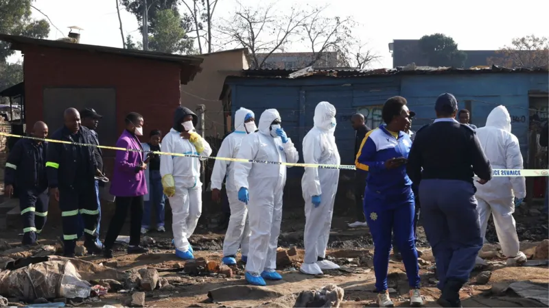 Police Launch Manhunt After Deadly Johannesburg Shooting Police in South Africa are searching for suspects after a violent attack in Johannesburg left 12 people dead and nine others injured. The incident took place in an informal settlement in the Cleveland area late Tuesday night. Authorities say a group of armed men arrived in the area and opened fire on residents before escaping in a vehicle. How the Attack Happened Police report that more than 10 armed suspects entered the Jumpers Informal Settlement. They moved through different parts of the community and fired on people at several locations. Officials say the attackers fled the scene in a white Toyota Quantum after carrying out the assault. Emergency services arrived after receiving reports of ongoing gunfire at around 23:10 local time. Police and medical teams found multiple victims at the scene. Casualties and Injuries Eight men and three women died at the location. One more victim died later in hospital due to severe injuries. Nine additional people were taken to nearby hospitals for treatment. Their condition has not been fully updated by authorities. Possible Motive Under Investigation Investigators have not confirmed a clear motive yet. However, police and local residents suspect the attack may be linked to disputes involving illegal mining groups operating in the area. Illegal mining has grown in parts of South Africa and is often connected to criminal networks and territorial conflicts. Police have described the attack as violent and deeply disturbing while continuing efforts to identify those responsible. Community and Police Response Residents of the informal settlement believe the violence may be connected to ongoing turf tensions. Police have not ruled out organized criminal activity. Law enforcement teams are reviewing evidence and following multiple leads to track down the suspects. A senior police official said the area remains under close investigation due to its proximity to illegal mining zones. Illegal Mining and Rising Violence Illegal mining continues to be a major concern in South Africa. It often takes place in abandoned mine areas where groups compete for control of resources. Authorities say such conflicts can escalate into violent confrontations that put local communities at risk.