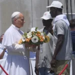Pope Leo XIV Visits Canary Islands to Highlight Migrant Sea Journeys Pope Meets Migrants in Gran Canaria Pope Leo XIV started his visit to the Canary Islands by meeting migrants in Gran Canaria. He listened to personal stories of people who crossed the Atlantic in unsafe conditions in search of a better life. He told them they are not just numbers or records but real human beings with dignity. He also said he bows in respect to their struggles and survival. Call for Safe Migration Routes During his visit, the Pope spoke about the need for legal and safe pathways for migration. He urged European leaders and societies not to become numb to deaths at sea. He warned that the oceans should not become silent graves for people trying to reach safety. He called on conscience and responsibility in handling migration policies. Tribute at Sea for Lives Lost At the port of Arguineguín in southern Gran Canaria, the Pope paid tribute to migrants who died during their journeys. He placed a wreath of flowers into the sea and prayed in silence. His message focused on remembering those who disappeared without any trace during Atlantic crossings. Dangerous Journey Across the Atlantic Data from the UNHCR shows that arrivals to Spain by sea have decreased this year. This decline is partly linked to stronger patrols along West African waters supported by European funding. Even with fewer arrivals, many migrants continue to attempt the journey. Many still lose their lives at sea. Survivor Story from The Gambia One survivor, Bakary Jaiju from The Gambia, shared his experience of crossing the Atlantic at age 19. He traveled in a wooden boat with around 160 people including women and children. He described a journey lasting seven days with very limited food and water. Fear was constant as passengers risked falling into the sea. Jaiju said he left his family behind because he wanted to improve their living conditions, even if it meant risking his life. Rescue and Life After Arrival When the boat ran out of fuel near El Hierro, Spanish rescue teams found and saved the passengers. After arrival, Jaiju spent three difficult months in a migrant camp. Later, he joined a support program in Tenerife to learn Spanish and work toward legal residence. A local parish priest known as Padre Pepe supports migrants through community programs that help them adjust and rebuild their lives.