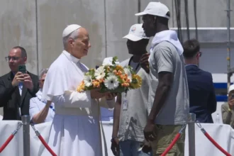 Pope Leo XIV Visits Canary Islands to Highlight Migrant Sea Journeys Pope Meets Migrants in Gran Canaria Pope Leo XIV started his visit to the Canary Islands by meeting migrants in Gran Canaria. He listened to personal stories of people who crossed the Atlantic in unsafe conditions in search of a better life. He told them they are not just numbers or records but real human beings with dignity. He also said he bows in respect to their struggles and survival. Call for Safe Migration Routes During his visit, the Pope spoke about the need for legal and safe pathways for migration. He urged European leaders and societies not to become numb to deaths at sea. He warned that the oceans should not become silent graves for people trying to reach safety. He called on conscience and responsibility in handling migration policies. Tribute at Sea for Lives Lost At the port of Arguineguín in southern Gran Canaria, the Pope paid tribute to migrants who died during their journeys. He placed a wreath of flowers into the sea and prayed in silence. His message focused on remembering those who disappeared without any trace during Atlantic crossings. Dangerous Journey Across the Atlantic Data from the UNHCR shows that arrivals to Spain by sea have decreased this year. This decline is partly linked to stronger patrols along West African waters supported by European funding. Even with fewer arrivals, many migrants continue to attempt the journey. Many still lose their lives at sea. Survivor Story from The Gambia One survivor, Bakary Jaiju from The Gambia, shared his experience of crossing the Atlantic at age 19. He traveled in a wooden boat with around 160 people including women and children. He described a journey lasting seven days with very limited food and water. Fear was constant as passengers risked falling into the sea. Jaiju said he left his family behind because he wanted to improve their living conditions, even if it meant risking his life. Rescue and Life After Arrival When the boat ran out of fuel near El Hierro, Spanish rescue teams found and saved the passengers. After arrival, Jaiju spent three difficult months in a migrant camp. Later, he joined a support program in Tenerife to learn Spanish and work toward legal residence. A local parish priest known as Padre Pepe supports migrants through community programs that help them adjust and rebuild their lives.