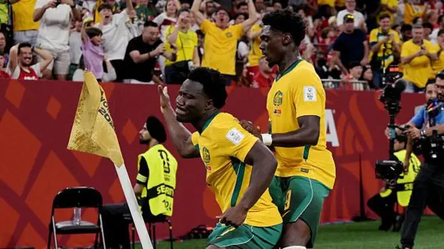 Nestory Irankunda World Cup Journey From Refugee Camp to Australia Star Early Life and Background Nestory Irankunda was born in a refugee camp in Tanzania in 2006. His parents had left Burundi because of war. Later, his family moved to Australia, where he grew up and found football as a passion. He worked his way up through youth football in Australia and joined Adelaide United. His performances quickly stood out because of his speed, skill, and direct attacking style. Rise at Adelaide United At Adelaide United, Irankunda made a strong impact in the A League. He scored 16 goals and added eight assists for the senior team. These numbers helped him build a reputation as one of Australia’s most exciting young players. His form attracted attention from top European clubs. That interest led to a big move to Germany. Move to Bayern Munich In 2024, Irankunda signed for Bayern Munich. He trained with world class players, including Harry Kane. However, he did not get first team minutes. This lack of game time created a problem. He wanted to play regularly to secure a place in Australia’s World Cup squad. To continue his growth, he went on loan to Grasshopper in Switzerland. Even there, he still needed more consistent playing time. Decision to Join Watford In 2025, Irankunda made a bold choice. He left Bayern Munich and joined Watford FC in England. He chose regular football over staying at a top European club. This decision helped him stay in contention for Australia’s national team. It also matched his long term dream of playing in England. International Breakthrough With Australia Irankunda made his Australia debut in a World Cup qualifier against Bangladesh. He scored his first international goals soon after, including a key strike against Palestine. He quickly became one of the youngest scorers in Australia’s football history. His confidence on the field grew with each match. Historic World Cup Moment In a major World Cup match against Turkey, Irankunda scored the opening goal in a 2 0 win. That goal made him the youngest player to score for Australia in a World Cup. The goal marked a turning point in his international career. It also showed why his decision to leave Bayern for more playing time worked out. Playing Style and Reputation Teammates describe him as fast, fearless, and unpredictable. Mohamed Toure called him “Houdini” because of his ability to escape defenders. Some believe he can have a big impact on Australia’s future, similar to top young stars in Europe. His growth now depends on consistency and discipline.