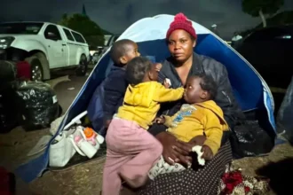 Migrants Face Rising Threats in South Africa as Protest Deadline Nears Violence and fear in Durban settlement A Malawian woman, Esnat Joseph, says armed men came to her home in Durban and ordered her family to leave South Africa. She says the attackers carried machetes and whips and injured her husband during the assault. He was taken to hospital with head and neck wounds. Joseph, who is 36, fled with her one year old triplets and now lives with thousands of other migrants in an open field in KwaZulu Natal. Around 7,000 foreign nationals, mostly from Malawi, have gathered there after leaving nearby informal settlements due to fear and intimidation. Growing pressure on undocumented migrants Tension has increased in parts of South Africa as groups linked to anti migrant demonstrations demand that undocumented foreigners leave the country by 30 June. Protesters, including members of March and March and ActionSA supporters, have staged marches and street gatherings in several areas. Chants of “Mabahambe,” meaning “they must go,” have become common during these demonstrations. While many of the protests have remained peaceful, migrants report threats and door to door intimidation in some communities. Government response and warnings President Cyril Ramaphosa has warned against targeting vulnerable people. He said blaming migrants is not a solution to deeper economic challenges facing the country. Authorities say some undocumented migrants are voluntarily leaving with support from their home countries. Malawi, Ghana, Mozambique, Nigeria and Zimbabwe have arranged transport for citizens who want to return home. Return and uncertainty Thousands have already returned through repatriation programs supported by consulates and donations. However, accounts from returnees suggest fear and rising hostility toward foreigners in some areas. Some migrants, like Benjamin, who recently returned to Nigeria after years in South Africa, say they no longer feel safe living there.