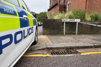 A 19 year old woman has died after gunshots were heard at a residential property in Dale Grove, Finchley, north London, shortly after midnight on Monday. Emergency services attended the scene after a call from the London Ambulance Service. When officers arrived, they found the woman with fatal injuries. She was pronounced dead at the location. Her family has been informed and is receiving support from specially trained officers. Emergency response at the scene Police secured the area soon after arriving at the property. The road was cordoned off while emergency teams worked at the scene. Authorities confirmed that formal identification has not yet taken place. A post mortem examination will be carried out to determine further details about the cause of death. Witness accounts from residents Local residents described shock and concern following the incident. One nearby resident, Geraldine Haren, said she was deeply surprised by what had happened. She described the area as calm and family friendly, adding that the community is close knit and usually peaceful. Another resident, Faz Saj, who lives on the same road with his family, said he returned home to find the street blocked. He said the incident felt unusual for the neighbourhood and expressed disbelief at what had taken place. Police investigation underway Detective Chief Inspector Allam Bhangoo is leading the investigation. He said officers are focused on establishing exactly what happened inside the property. He also expressed sympathy for the victim’s family during what he described as an extremely difficult time. Police confirmed that no arrests have been made so far. Officers are continuing to gather evidence and speak to potential witnesses. Authorities expect an increased police presence in the area over the coming days as enquiries continue. Residents have been encouraged to speak with officers if they have any concerns or information. Community reaction The incident has left the local community in shock. Residents described the neighbourhood as usually quiet and safe, making the sudden violence even more distressing. Many people living nearby said they are struggling to understand how such an event could happen in their area. Next steps in the case Investigators will continue examining forensic evidence and witness statements. A post mortem examination will provide further medical details, which may help clarify the sequence of events. Police have stated that updates will be shared once more verified information becomes available.