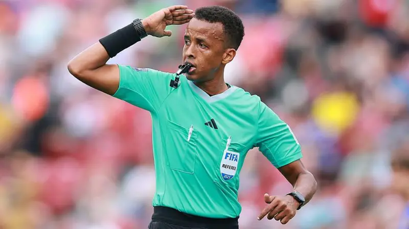 Somali Referee Omar Artan Denied Entry to US Despite Valid Visa Somali referee Omar Abdulkadir Artan has been denied entry into the United States ahead of the World Cup, even though he says he had valid travel documents and a proper visa. He was set to become the first Somali referee to officiate at a World Cup finals. However, he was stopped at Miami International Airport and sent back after an extended immigration process. Long Immigration Interview Before Repatriation Artan said immigration officials held him for an 11 hour interview upon arrival. After that, he was placed in a separate holding area for several hours. Later, he was put on a flight back to Istanbul. No official reason for the decision has been shared by US authorities. FIFA Confirms Removal from Tournament The global football governing body confirmed that Artan will not take part in the tournament. FIFA stated that host country immigration processes are outside its control. It added that officials were informed his entry status would not change. Because of tournament rules, he cannot continue training or officiating even at matches held outside the United States. Training Base Requirements in Miami All referees selected for the World Cup are required to stay at a training base in Miami. This setup is part of preparation and security planning for match officials. Refereeing chief Pierluigi Collina has organized this centralized training system for officials taking part in the tournament. Claims of Valid Documents and Visa Artan insisted that he had all required documents, including a valid visa and supporting travel papers. A Somali sports official also confirmed that he was traveling with proper authorization. Reports say a diplomatic passport had been arranged to support his travel after earlier visa issues. Political Context Around Immigration Rules The case comes amid stricter immigration rules affecting several countries, including Somalia. Earlier remarks from US leadership indicated concerns about Somali immigration, which has added sensitivity to the situation. Artan said he felt disappointed, adding that refereeing at the World Cup was the biggest dream of his career.