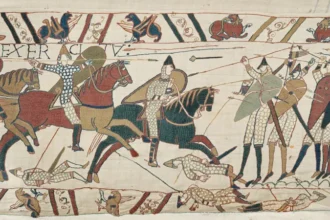 Bayeux Tapestry Returns to UK After 900 Years Under Heavy Security The famous Bayeux Tapestry has arrived in the United Kingdom for the first time in almost 900 years. The historic 11th century artwork reached the British Museum under strict police protection after being transported from northern France. The 70 metre long embroidered masterpiece shows 58 detailed scenes from the events before the Battle of Hastings and the Norman Conquest of England in 1066. The battle changed the future of England and remains one of the most important moments in British history. Historic Arrival at the British Museum The valuable artwork arrived at 02:50 BST in a specially protected transport vehicle. A large secure crate containing the tapestry was carefully removed from the lorry at the British Museum loading area. Museum officials, including British Museum director Nick Cullinan and the French ambassador to the UK, attended the historic arrival. Cullinan described the moment as extraordinary and said the museum was excited to share the rare artwork with visitors from around the world. The exhibition team also expressed their emotions during the arrival. Millie Horton Insch, the project curator for the exhibition, said seeing such an important historical object arrive was a deeply meaningful experience. A Masterpiece From the 11th Century The Bayeux Tapestry is not a traditional painting. It is a detailed embroidery that tells the story of William the Conqueror’s journey and the events that led to the Norman takeover of England. Historians believe the artwork was created shortly after the Battle of Hastings. It provides a unique view of medieval life, warfare, ships, soldiers, and political events from nearly 1,000 years ago. The British Museum will place the tapestry on public display in September, allowing visitors to experience one of the world’s most important historical treasures. France and UK Celebrate Cultural Friendship French President Emmanuel Macron described the loan as a symbol of friendship between France and the United Kingdom. He called it a sign of trust and cooperation between the two countries. To celebrate the occasion, the British Museum displayed a projection of the tapestry on the White Cliffs of Dover with the French message “Merci” as a gesture of appreciation. Concerns Over Moving the Historic Artwork Although many people welcomed the exhibition, some concerns were raised in France about transporting such a fragile object. A French petition argued that moving the tapestry could put the historic item at risk. Some experts and artists also questioned whether the artwork should travel due to its age and delicate condition. Despite these concerns, the Bayeux Tapestry has now safely reached the UK, where it will become one of the most significant historical exhibitions of the year.