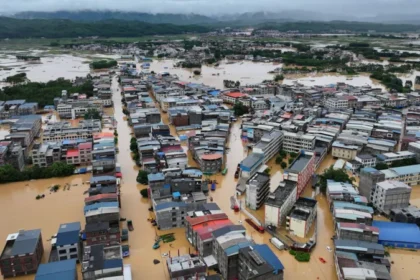 Typhoon Maysak Floods China After Heavy Rain Breaks Dam Wall Fast Rising Floodwaters Force Villagers to Escape Heavy rainfall from Typhoon Maysak caused severe flooding in Renhe village, located in Guangxi province, southern China. The rain started on Sunday, but residents did not expect the situation to become dangerous so quickly. Within hours, rising water entered homes and covered streets. By early Monday morning, floodwater reached knee level. Later, it completely covered the first floors of many houses. Residents said the water moved faster than expected. Many families escaped without taking food or important belongings because they had little time to react. A local resident named Zhou said the flood arrived suddenly and forced villagers to leave their homes immediately. Dam Damage and Rising River Levels Create Crisis Typhoon Maysak caused rivers across Guangxi to overflow. The powerful storm also damaged dam walls, increasing the danger for nearby communities. Thousands of people have left their homes as rescue teams continue operations in flooded areas. Several villages and parts of Nanning city faced serious water damage. Some residents waited on rooftops and called for help as floodwater surrounded their homes. Officials reported that the storm caused deaths and injuries across different regions. Rescue workers continue searching affected areas and providing emergency support. Extreme Weather Spreads Across China The storm also brought dangerous weather conditions to other parts of China. Hubei province experienced strong thunderstorms and rare tornado activity hundreds of kilometres away from Guangxi. The severe weather damaged communities and disrupted daily life for many residents. Chinese President Xi Jinping ordered emergency teams to increase rescue and relief operations. Authorities in Nanning warned that more heavy rain could make rescue work difficult. Climate Concerns Increase After Severe Storm Typhoons often bring heavy rainfall to China during this period of the year. However, experts say stronger extreme weather events have become a growing concern due to climate change. China’s agriculture sector, worth trillions of dollars, faces increasing risks from floods, storms, and changing weather patterns. Typhoon Maysak marks the first major storm to hit China during the 2026 typhoon season. Officials described the storm as sudden and powerful, with intense winds and short periods of extreme rainfall. More Storm Threats Ahead Weather experts are also monitoring another powerful storm, Super Typhoon Bavi, which could affect China’s eastern coastline later this week. Authorities continue to prepare emergency plans as communities recover from the destruction caused by Typhoon Maysak. The disaster highlights the growing need for stronger flood protection systems and faster emergency responses to protect people living in high risk areas.