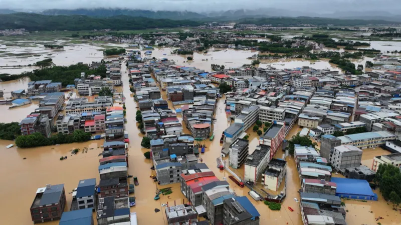 Typhoon Maysak Floods China After Heavy Rain Breaks Dam Wall Fast Rising Floodwaters Force Villagers to Escape Heavy rainfall from Typhoon Maysak caused severe flooding in Renhe village, located in Guangxi province, southern China. The rain started on Sunday, but residents did not expect the situation to become dangerous so quickly. Within hours, rising water entered homes and covered streets. By early Monday morning, floodwater reached knee level. Later, it completely covered the first floors of many houses. Residents said the water moved faster than expected. Many families escaped without taking food or important belongings because they had little time to react. A local resident named Zhou said the flood arrived suddenly and forced villagers to leave their homes immediately. Dam Damage and Rising River Levels Create Crisis Typhoon Maysak caused rivers across Guangxi to overflow. The powerful storm also damaged dam walls, increasing the danger for nearby communities. Thousands of people have left their homes as rescue teams continue operations in flooded areas. Several villages and parts of Nanning city faced serious water damage. Some residents waited on rooftops and called for help as floodwater surrounded their homes. Officials reported that the storm caused deaths and injuries across different regions. Rescue workers continue searching affected areas and providing emergency support. Extreme Weather Spreads Across China The storm also brought dangerous weather conditions to other parts of China. Hubei province experienced strong thunderstorms and rare tornado activity hundreds of kilometres away from Guangxi. The severe weather damaged communities and disrupted daily life for many residents. Chinese President Xi Jinping ordered emergency teams to increase rescue and relief operations. Authorities in Nanning warned that more heavy rain could make rescue work difficult. Climate Concerns Increase After Severe Storm Typhoons often bring heavy rainfall to China during this period of the year. However, experts say stronger extreme weather events have become a growing concern due to climate change. China’s agriculture sector, worth trillions of dollars, faces increasing risks from floods, storms, and changing weather patterns. Typhoon Maysak marks the first major storm to hit China during the 2026 typhoon season. Officials described the storm as sudden and powerful, with intense winds and short periods of extreme rainfall. More Storm Threats Ahead Weather experts are also monitoring another powerful storm, Super Typhoon Bavi, which could affect China’s eastern coastline later this week. Authorities continue to prepare emergency plans as communities recover from the destruction caused by Typhoon Maysak. The disaster highlights the growing need for stronger flood protection systems and faster emergency responses to protect people living in high risk areas.